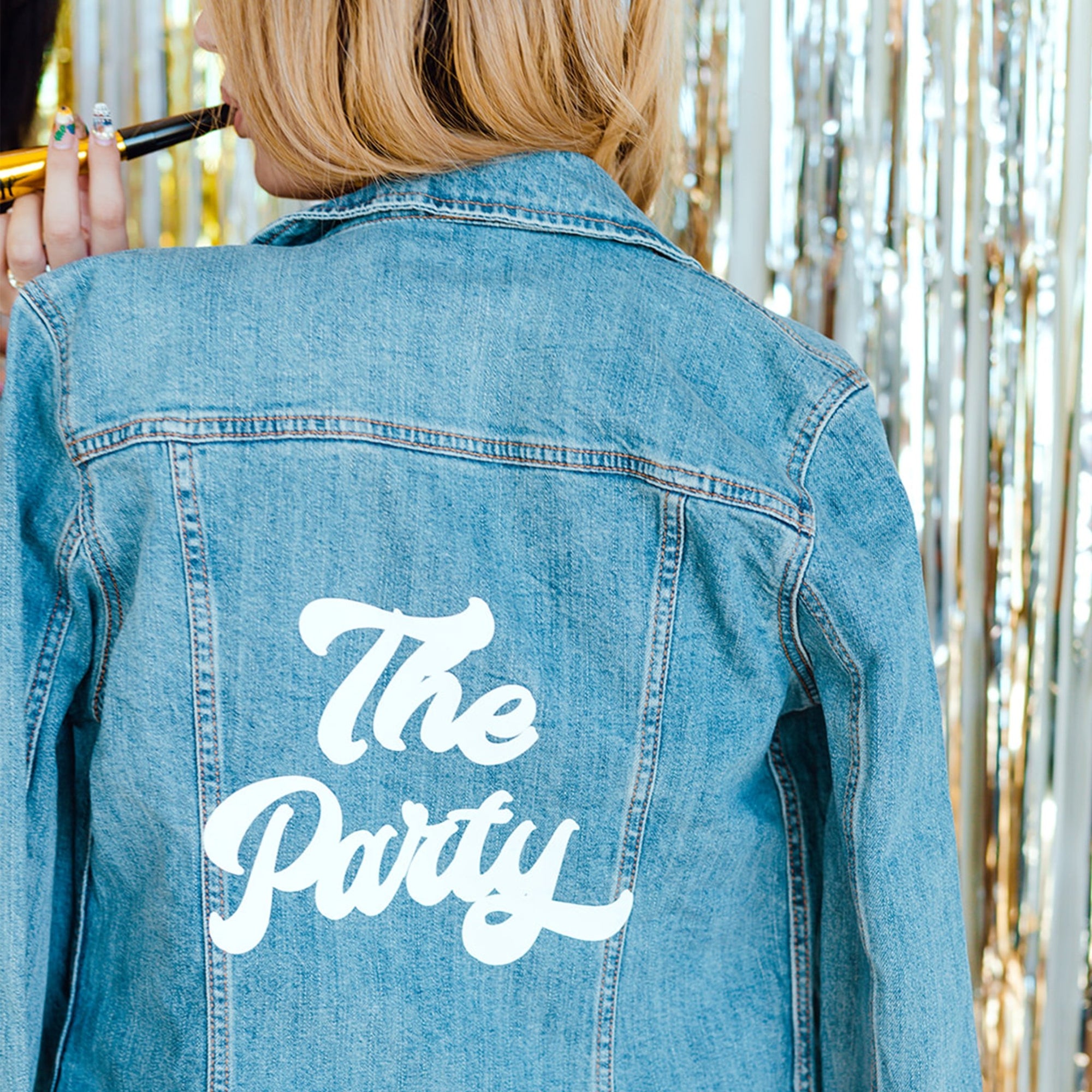 A woman wears a customized jean jacket that says "The Party" in white.