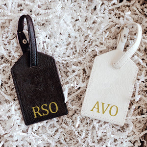 A set of black and white luggage tags are monogrammed with gold metallic.