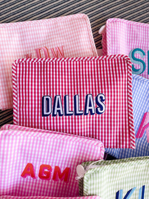 An assortment of embroidered gingham pouches are customized with different of name and monograms