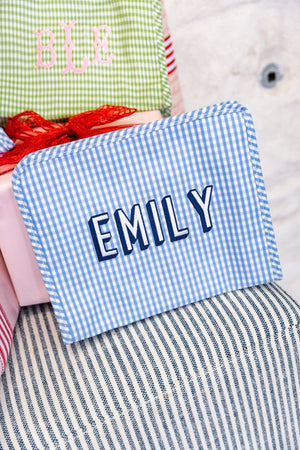 A blue gingham pouch is embroidered with a name in white and navy thread.