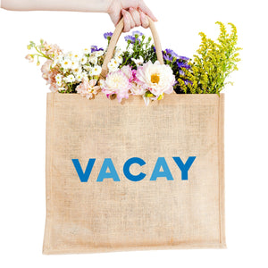 A jute tote reads "VACAY" across the front in blue letters