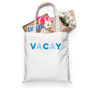 A white cotton tote reads "VACAY" across the front in blue letters