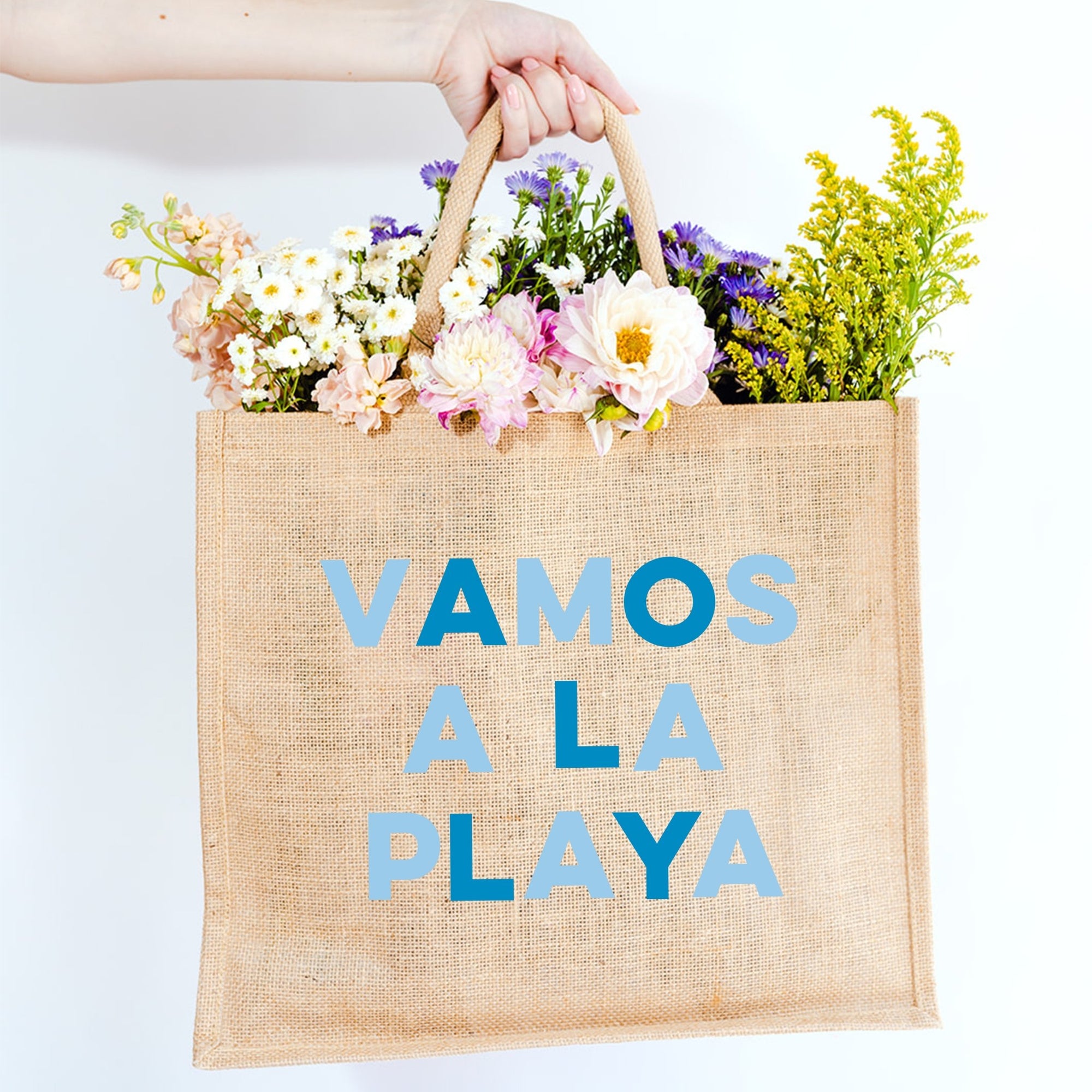 A jute tote reads "VAMOS A LA PLAYA" across the front in red and pink letters