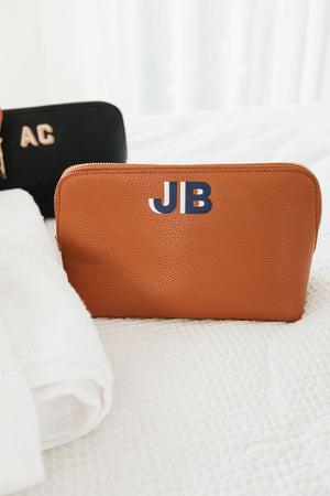 A tan leather pouch is customized with a navy and white monogram.