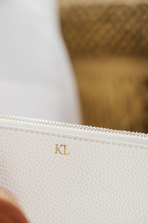 A white leather pouch is personalized with a gold foil monogram.