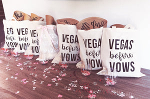 A group of totes which read "Vegas Before Vows" are lined up and filled with goodies.