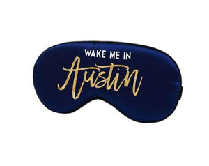 A navy sleep mask is customized with a gold sparkly design that says "Wake Me In Austin".