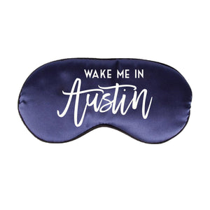 A navy sleep mask is customized with a white design that says "Wake Me In Austin".