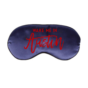 A navy sleep mask is customized with a red design that says "Wake Me In Austin".