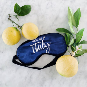 A navy sleep mask is customized with "Wake Me In Italy" in white.