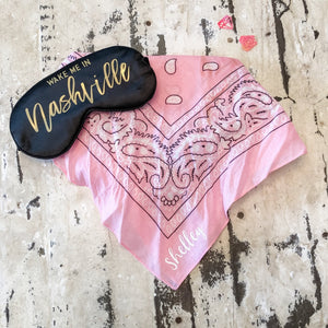 A pink bandana is customized with a name and placed with a black sleep mask which says "Wake Me In Nashville".