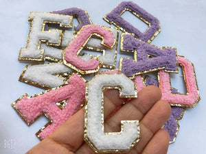 An array of patch letters is put into a pile to show off their bright color and gold glitter outline.
