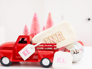 A red toy truck holds a white corduroy pouch customized with patches alongside a monogrammed luggage tag and jewelry case.