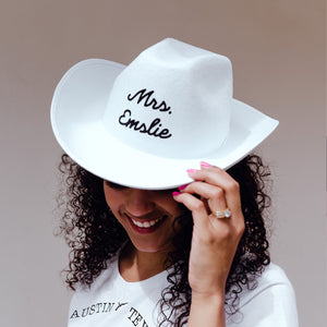 A woman wears a white cowboy hat that is customized with her last name.