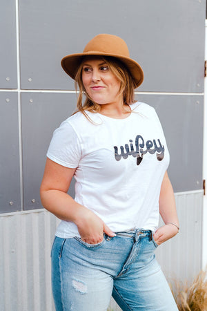 A woman wears a white t-shirt that reads "Wifey"